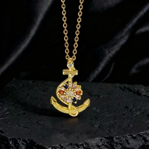Detalle del collar con colgante de ancla dorado y gemas de colores sobre piedra negra