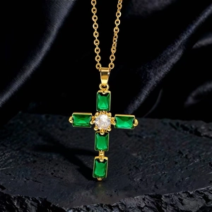 Dettaglio della collana a croce dorata con cristalli verdi smeraldo su sfondo di seta nera