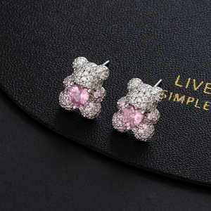 Sparkling teddy bear stud earrings with pink heart gemstone on black leather texture