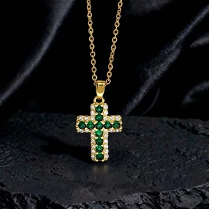 Dettaglio del ciondolo a croce con zircone verde e diamanti bianchi su catena d'oro