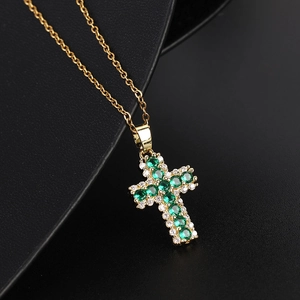 Collana a croce dorata con pietra verde smeraldo e zirconi su fondo nero materico
