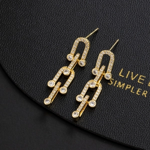 Minimalist gold U-link drop earrings with pavé zircons on black leather background
