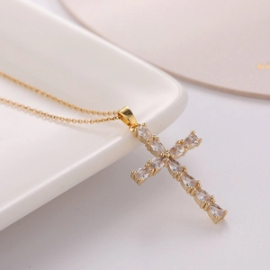 Gold-plated cross necklace with sparkling pear-cut cubic zirconia on a white porcelain tray
