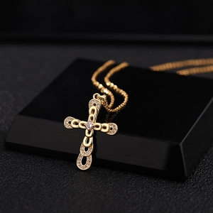 Close-up of gold plated cross pendant with cubic zirconia on a black reflective stand