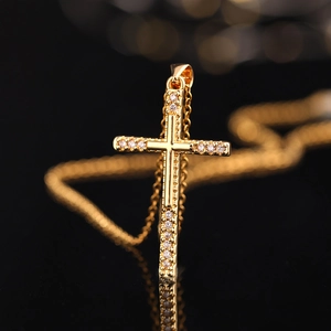 Makroaufnahme von Goldkreuz-Anhänger mit Zirkonia-Besatz und Spiegelung auf schwarzem Grund