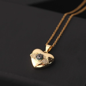 Detalle del colgante corazón dorado con ojo de circón verde sobre fondo oscuro
