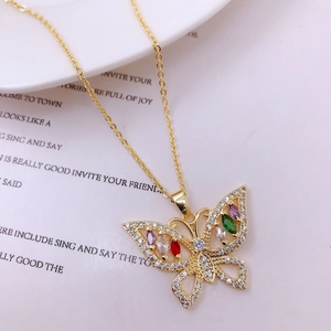Close-up of golden butterfly pendant with colorful zircon stones on ceramic plate