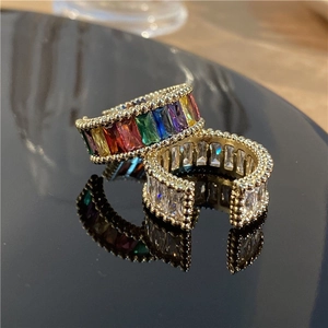 Close-up of rainbow zircon gold open rings with micro-beaded edges on reflective black surface