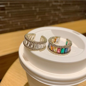 Adjustable gold C-shape rings with rainbow and clear cubic zirconia on a white surface