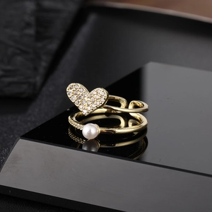 Double-layered gold ring with heart crystal and white pearl on minimalist black display