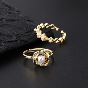 Close-up of gold-plated open rings with pearls and rhinestones on black texture