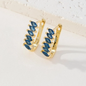 Détail de boucles d'oreilles dorées 18K avec zircons bleus en forme de trèfle chic