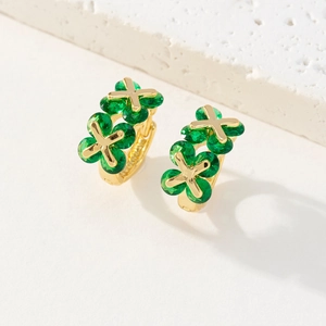Détail de boucles d'oreilles huggie dorées 18K avec trèfles verts et motifs d'étoiles