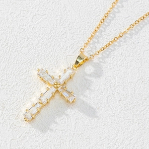Elegant gold cross necklace with rectangular zircon inlay on white textured background