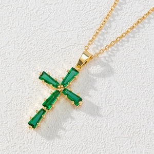 Macro shot of gold cross pendant with emerald green baguette zircons on delicate chain