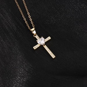 Dettaglio macro del ciondolo a croce in oro 18K con zircone a cuore su sfondo nero