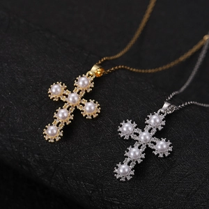 Dettaglio macro di ciondoli a croce con perle e zirconi placcati in oro e argento