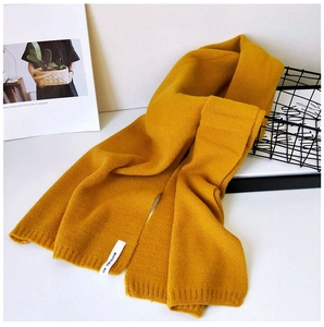 Detail eines senfgelben Strickschals mit Rippenmuster und weißem minimalistischem Label