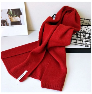 Detail eines roten Strickschals mit Rippenstruktur und weißem Etikett auf weißem Grund