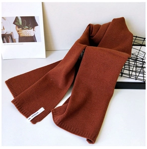 Nahaufnahme eines karamellfarbenen Strickschals mit dekorativem Markenlabel und Wolltextur
