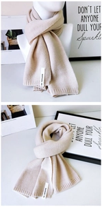 Detail eines beigen Strickschals mit Markenetikett und feiner Rippenstruktur