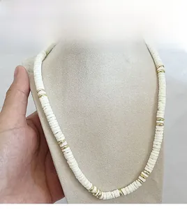 Détail du collier de coquillages bohème avec anneaux dorés sur un support d'exposition beige