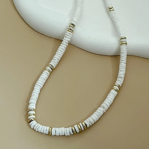 Collier de perles Heishi blanches avec espaceurs dorés sur fond beige artistique
