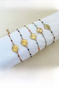 Detail of five gold Yin Yang charm bracelets with colorful beads on a white display