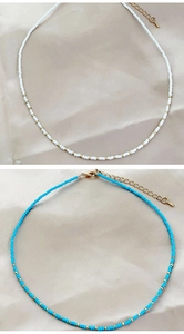Close-up of white and light blue beaded necklaces with gold metal accents on silk fabric