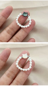 Detailed view of elastic pearl rings featuring minimalist black and white shell cat charms