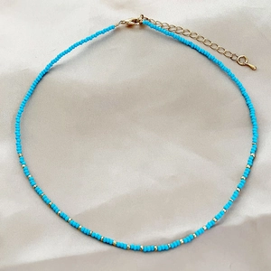 Minimalist turquoise beaded choker necklace with gold accents on soft beige satin