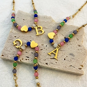 Colorful beaded necklace set with gold letter pendants on natural stone background