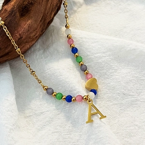 Colorful beaded necklace with gold A-letter and heart pendant on white fabric