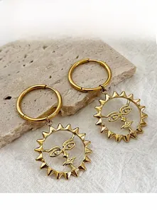 Macro shot of gold sun face drop earrings featuring sunface charms on stone background