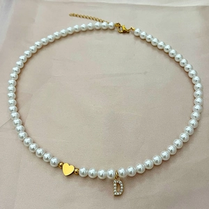 Elegante collar de perlas con colgante de corazón dorado y letra D brillante sobre seda rosa