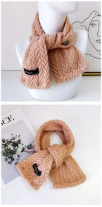 Détail d'une écharpe en maille beige avec motif torsadé, bouton et étiquette tissée