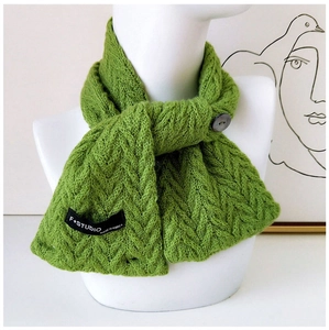 Détail de l'écharpe en maille torsadée verte avec bouton noir et étiquette studio
