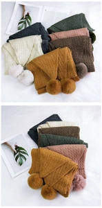 Close-up of thick knitted scarf showing cable knit textures and plush faux fur pom-poms