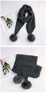 Detailed knit texture of dark grey scarf with large fluffy pom-poms on the ends