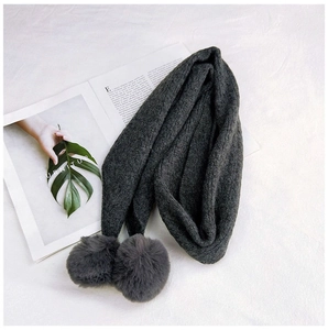 Detail of dark grey knit scarf featuring thick yarn texture and plush pom-poms