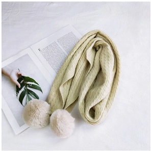 Macro detail of the thick cable knit texture and soft plush pom-poms on the beige winter scarf