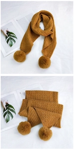 Detail of cable knit pattern and large fluffy pom-poms on a mustard yellow scarf