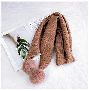 Detail view of caramel knitted scarf with soft pink pom poms and textured knit pattern