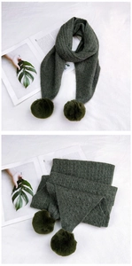 Detail of dark green knit scarf showing vertical stripes and fluffy pom-pom accents