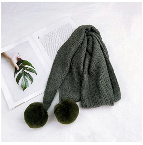 Detailed knit texture of dark green scarf featuring two fluffy matching pom-poms
