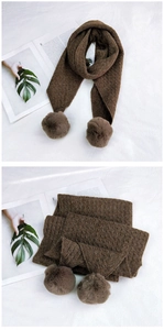 Close-up of dark brown knitted scarf featuring chunky cable patterns and faux fur pom-poms