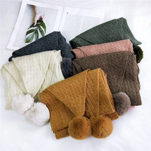 Knitted scarf with double pom-poms in various colors featuring thick cable-knit texture
