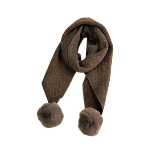Dark brown knit scarf with plush pom-poms and cable stitch pattern on white background