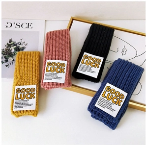 Close-up of four knitted wool scarves in yellow, pink, blue and black with Good Luck labels