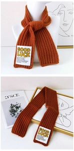 Detail of burnt orange knit scarf with vertical ribbing and GOOD LUCK patch label